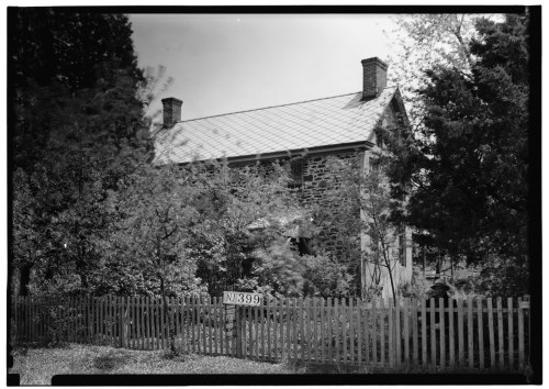 A historic stone house surrounded by trees, with a white picket fence and a sign reading "NJ 399."