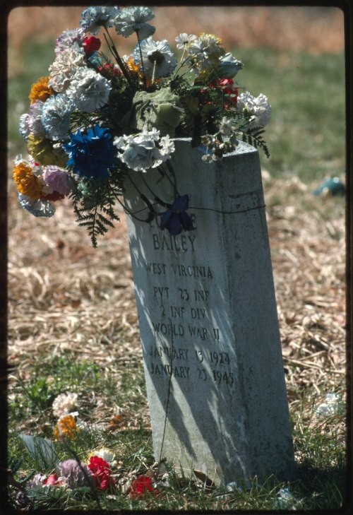 A gravestone adorned with colorful flowers, honoring a WWII soldier named Bailey from West Virginia.