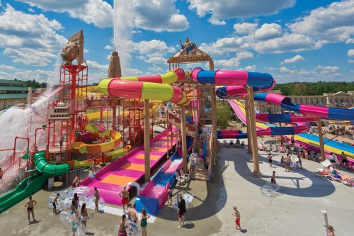 A vibrant water park with colorful slides, pools, and families enjoying the attractions under a blue sky with clouds.
