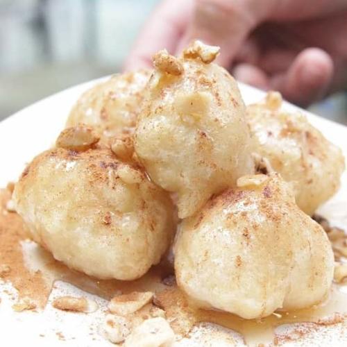 A plate of five golden, round dumplings topped with crushed nuts and a dusting of cinnamon.