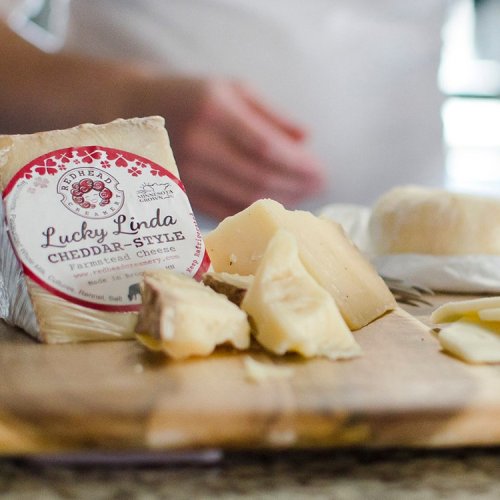 A close-up of cheese blocks and slices on a wooden board, with a hand reaching for a piece.