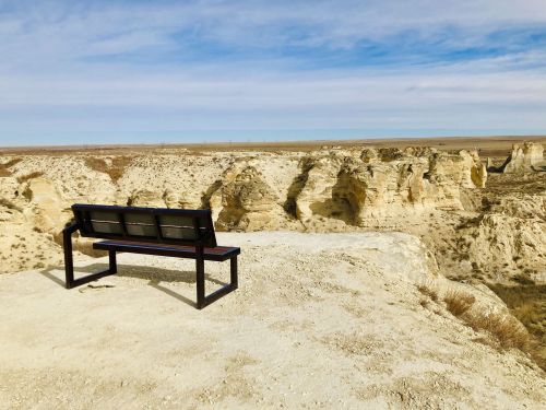 A wooden bench overlooks a vast, rocky landscape under a blue sky, offering a serene view of the cliffs.
