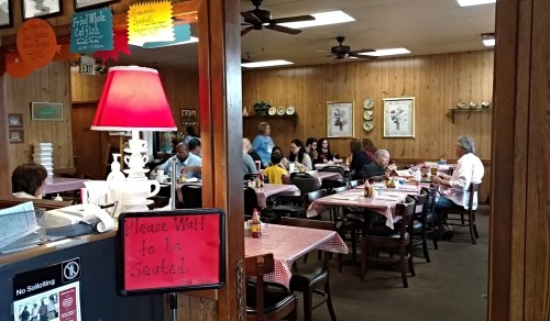A cozy restaurant interior with wooden walls, tables set with checkered tablecloths, and diners enjoying their meals.