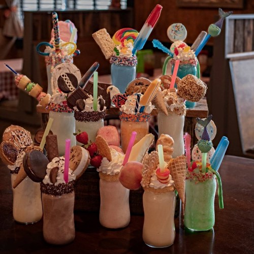 A colorful display of extravagant milkshakes topped with candies, cookies, and various treats in mason jars.