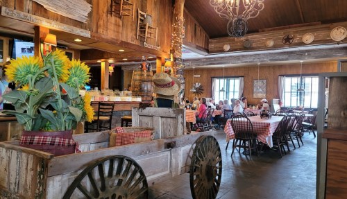 A rustic restaurant interior with wooden decor, checkered tablecloths, and sunflowers in a wagon centerpiece.