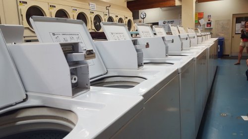 A row of white washing machines in a laundromat, with a person in the background.