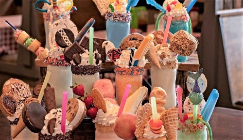 A colorful display of extravagant milkshakes topped with cookies, candies, and whipped cream in various jars.