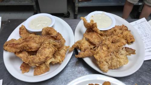 Two plates of crispy fried chicken tenders served with dipping sauce on the side.