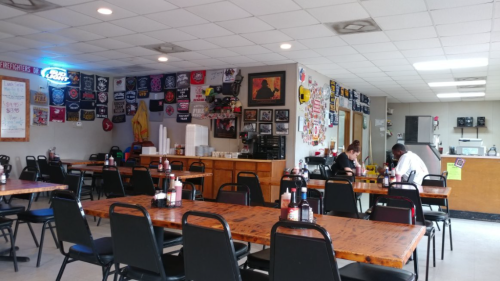 Interior of a casual restaurant with wooden tables, black chairs, and walls decorated with various posters and memorabilia.