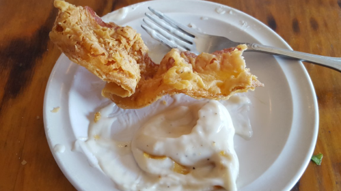 A piece of fried chicken on a plate with a fork and a dollop of creamy sauce.