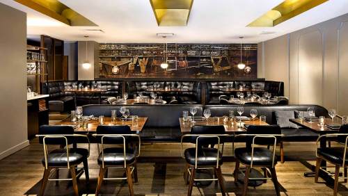 Modern restaurant interior featuring black leather seating, wooden tables, and stylish lighting.