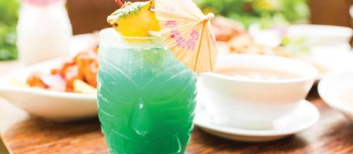 A tropical cocktail with a pineapple slice and a small umbrella, set against a blurred background of food.