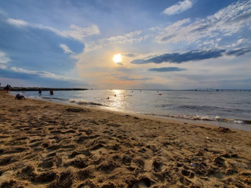 A serene beach scene at sunset, with gentle waves lapping at the shore and a cloudy sky reflecting warm colors.