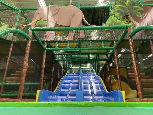 Colorful indoor playground featuring slides, climbing structures, and an elephant mural in the background.