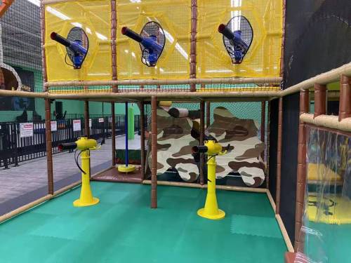 A colorful indoor play area featuring yellow netted structures and toy cannons on a green floor.