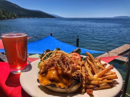 A delicious cheeseburger with fries and a drink, set against a scenic lake view on a sunny day.