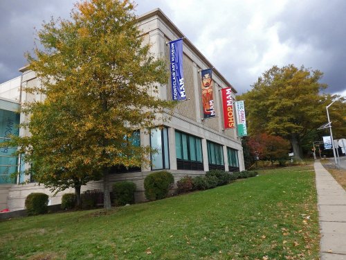 A building with banners, surrounded by trees and grass, under a cloudy sky.