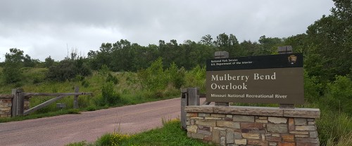 Sign for Mulberry Bend Overlook at Missouri National Recreational River, with a cloudy sky and green landscape in the background.