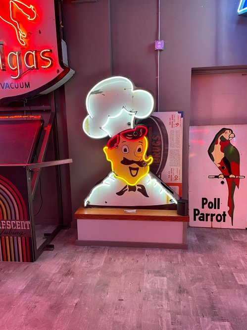 A colorful neon sign of a smiling chef with a red hat and mustache, displayed in a retro-themed setting.