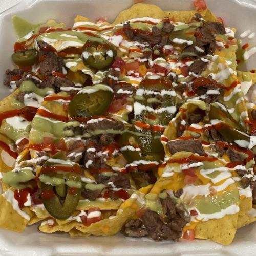 A plate of nachos topped with beef, jalapeños, diced tomatoes, and drizzles of sour cream and sauces.