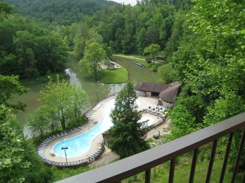Aerial view of a lush green landscape featuring a pool, a river, and a building surrounded by trees.