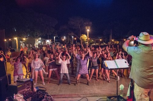 A lively crowd dances outdoors at night, enjoying a performance with colorful lights and a musician in the foreground.