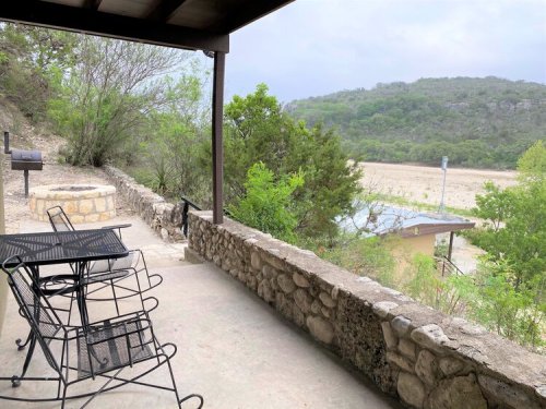 A stone patio with metal chairs overlooks a green landscape and distant hills under a cloudy sky.