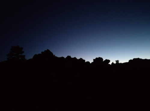 Silhouette of rocky terrain against a dark blue sky at dusk, with faint light on the horizon.