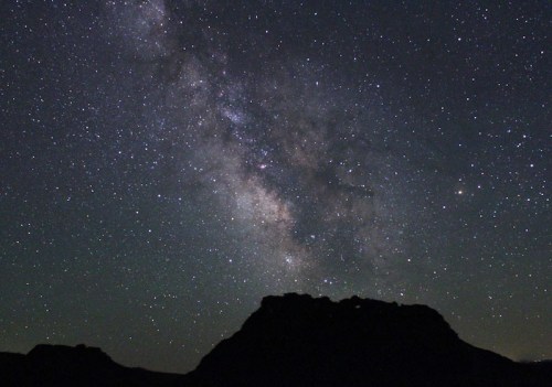 A starry night sky featuring the Milky Way above a dark silhouette of a mountain.