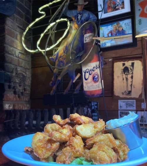 A plate of golden fried food with a side of dipping sauce, set against a rustic bar backdrop with neon signs.