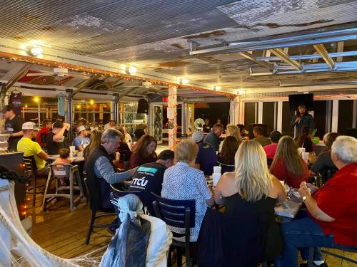 A lively indoor gathering at a bar with people seated, enjoying drinks and entertainment in a cozy atmosphere.