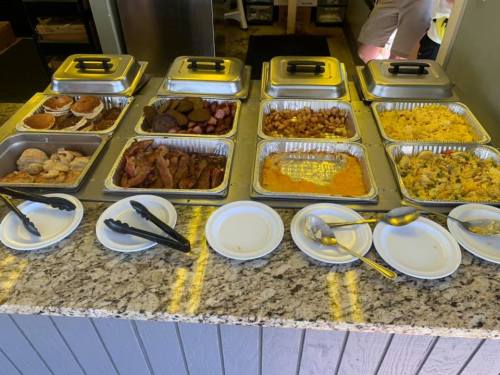 A buffet spread featuring various dishes in metal trays, including meats, sides, and breakfast items on a countertop.