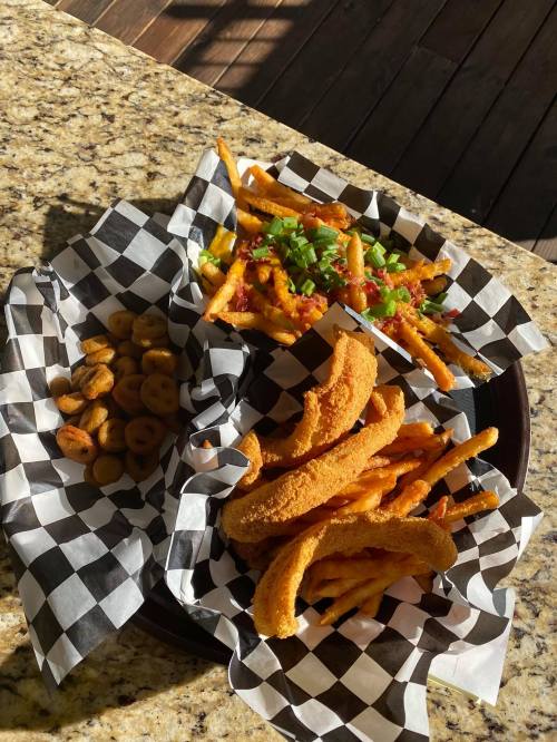 A plate with two servings of fries topped with green onions and chili, and a side of crispy banana chips.