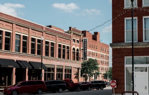 Historic buildings line a street with parked cars, featuring a marquee sign and clear blue skies above.
