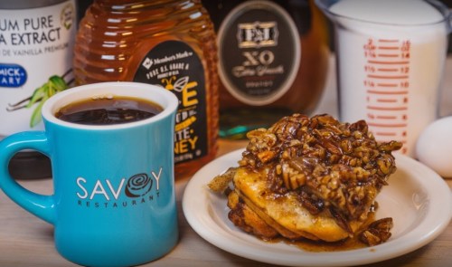 A blue mug of coffee beside a plate of pecan-topped dessert, honey, vanilla extract, and measuring cup in the background.