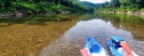 Two kayaks on a calm, clear river with lush green trees and hills in the background.