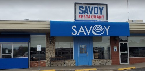 Exterior of Savoy Restaurant featuring a blue awning and a stone facade, with a sign above displaying the restaurant's name.