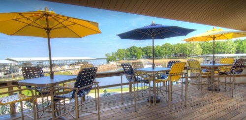 Outdoor seating area with yellow and blue umbrellas overlooking a calm waterway and lush greenery.