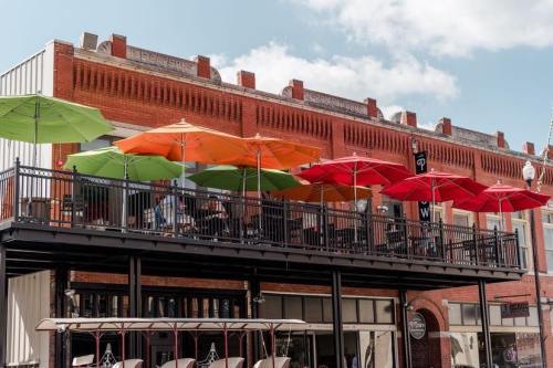A vibrant outdoor patio with colorful umbrellas on a sunny day, overlooking a historic brick building.