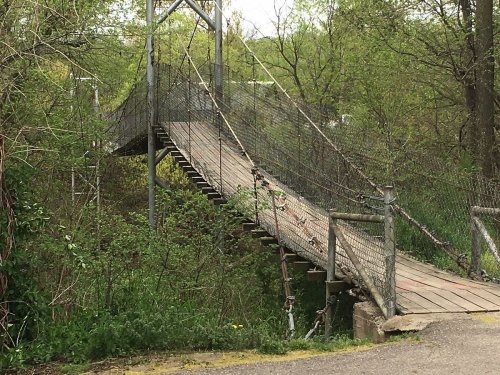 A weathered wooden suspension bridge surrounded by lush greenery and trees.