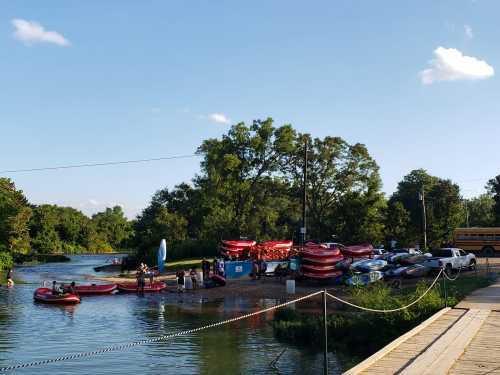 A group of people preparing kayaks and canoes by a river, with trees and a school bus in the background.