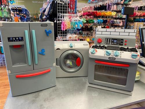 A set of toy kitchen appliances including a refrigerator, washing machine, and stove, displayed on a table.