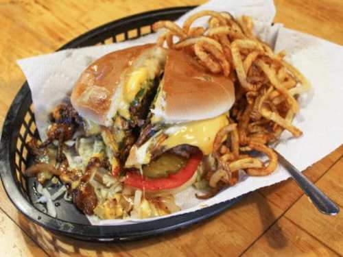 A juicy cheeseburger with melted cheese, pickles, and tomato, served with a side of curly fries on a black basket.