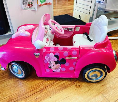 A pink toy car with polka dots and a Minnie Mouse design, featuring a white seat and steering wheel.