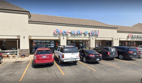 Storefront of "Once Upon a Child" with parked cars in front, clear blue sky above.