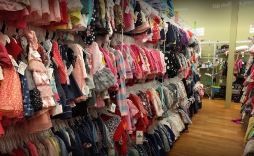 A colorful aisle of children's clothing, featuring various dresses and outfits hanging on racks.