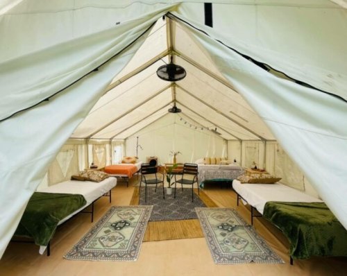 Interior of a spacious tent with beds, a table, and decorative rugs, creating a cozy, inviting atmosphere.