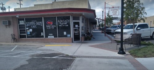 A street view of Stepping Stone Café with an "Open" sign, featuring outdoor seating and nearby vehicles.