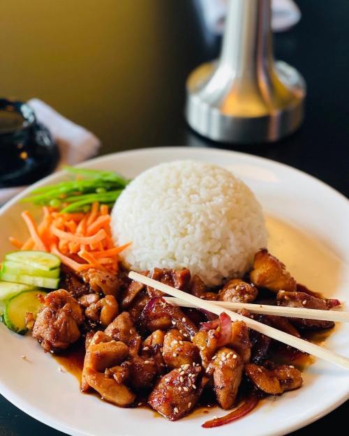 A plate of chicken with sauce, rice, and fresh vegetables, garnished with chopsticks.