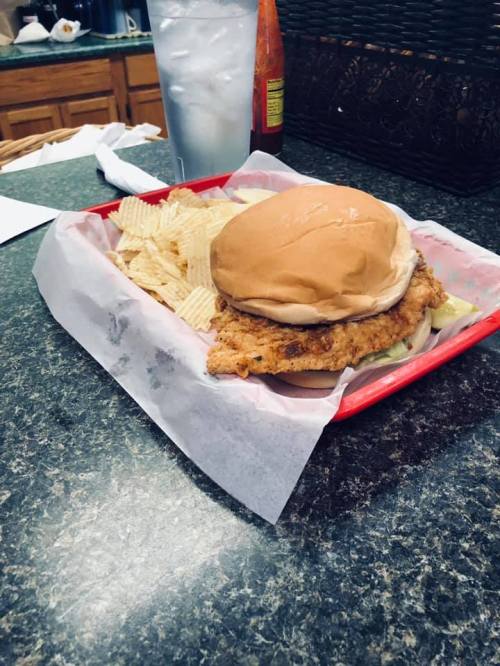 A fried chicken sandwich on a bun with lettuce, served with a side of potato chips in a red tray.